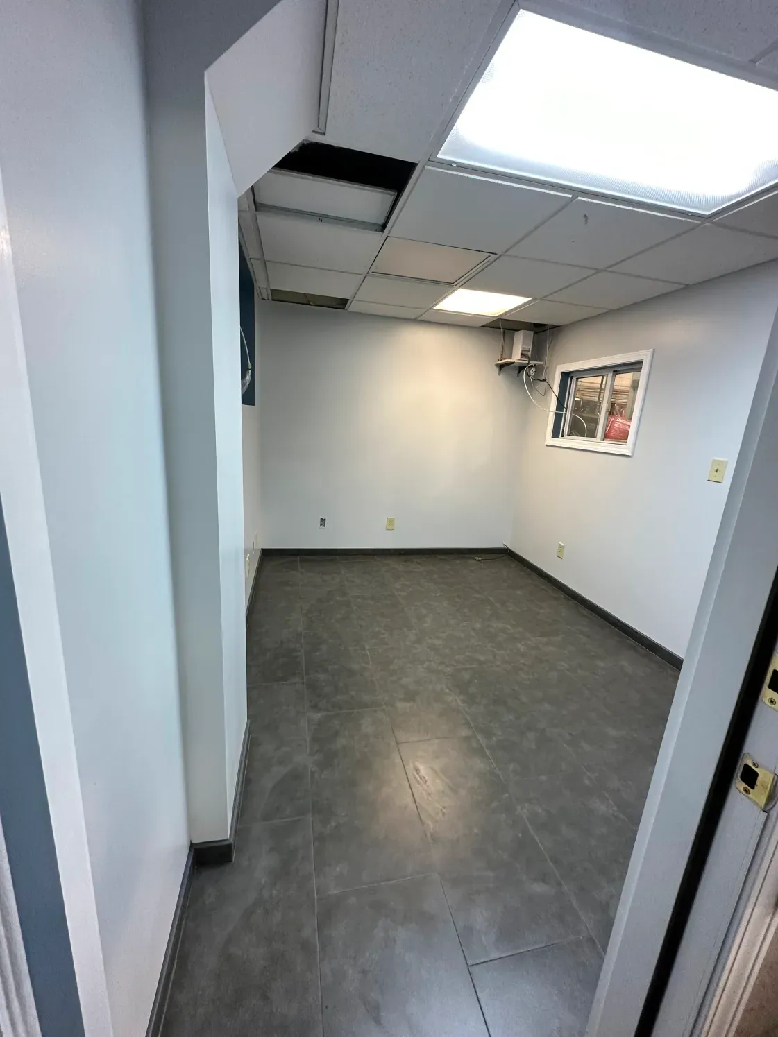 Empty office room with gray tile floor, white walls, and a window.