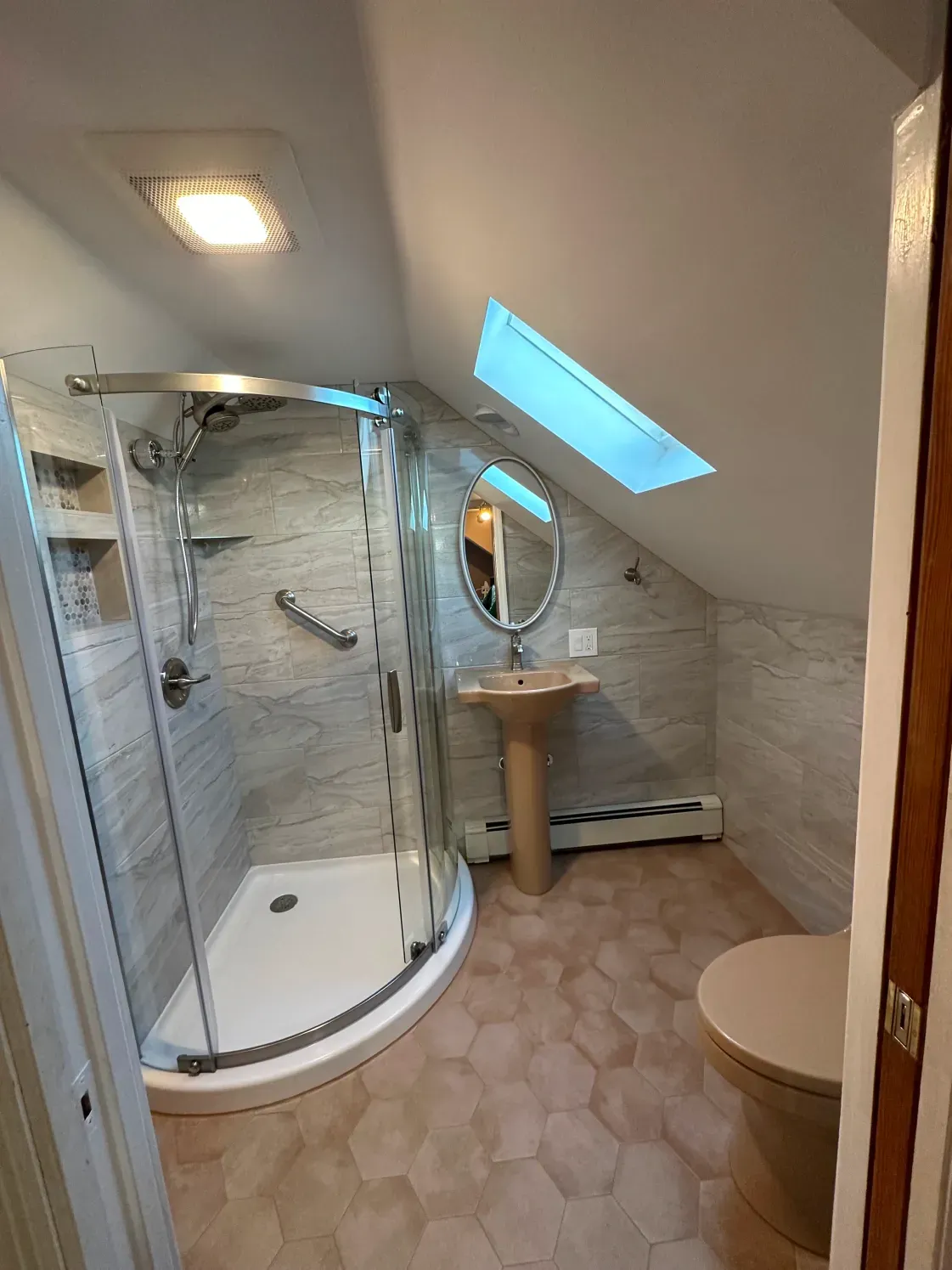 Small bathroom with a curved glass shower, pedestal sink, and toilet under a skylight.