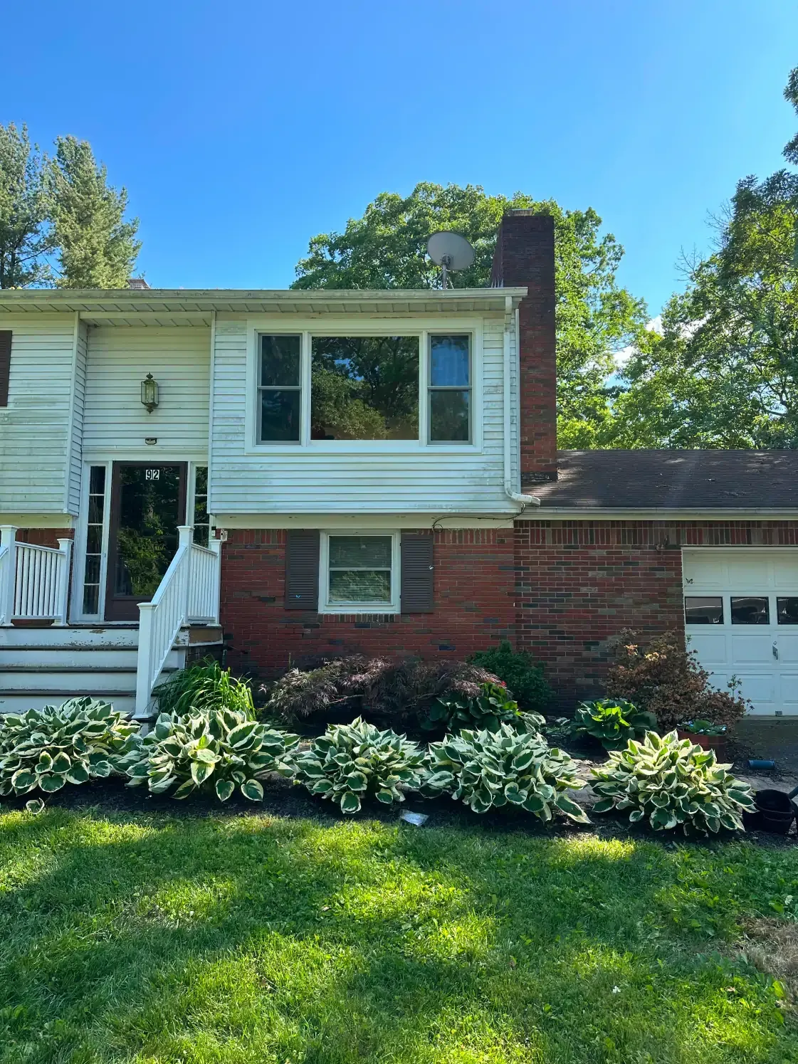 Split-level house with brick facade and white siding; lush green and white hostas in front.