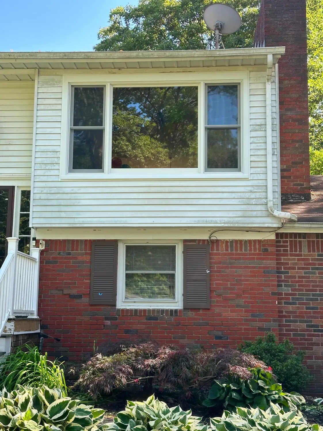 Exterior view of a house with white siding on top, brick on the bottom, and windows.