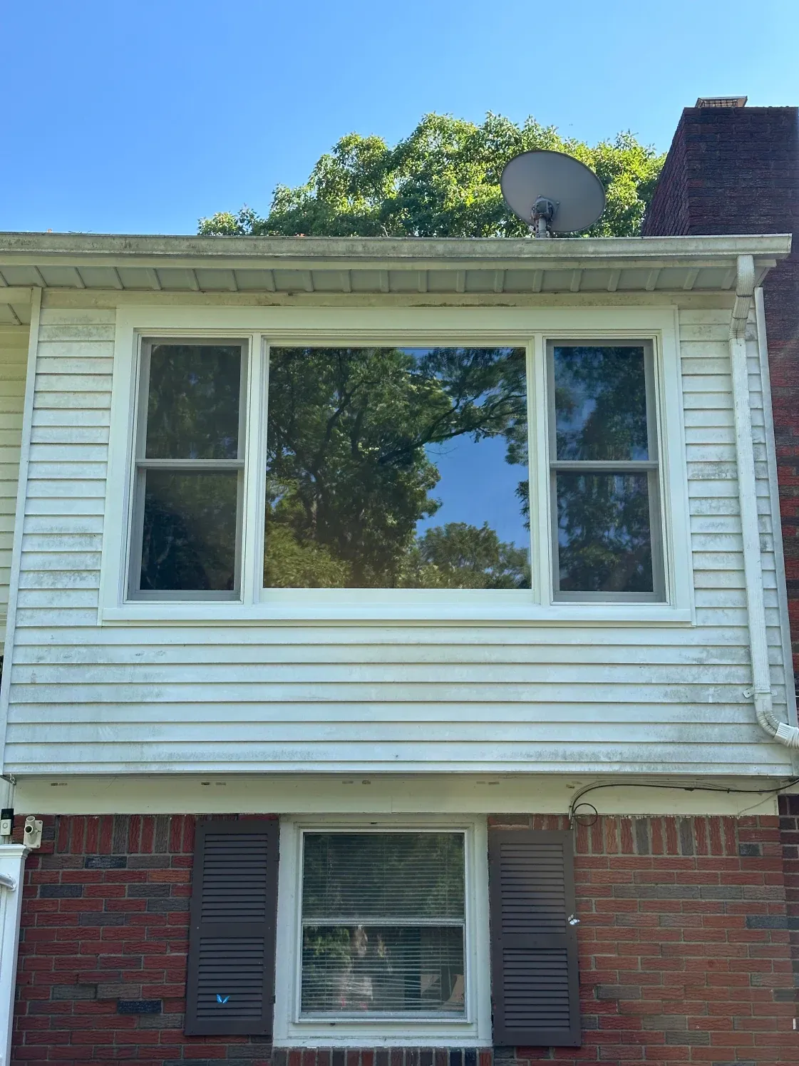 Exterior of a two-story house with white siding and brick, featuring multiple windows.