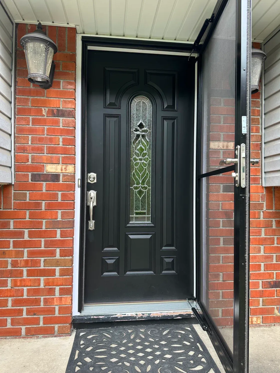 Black front door with glass, open screen door, brick exterior.