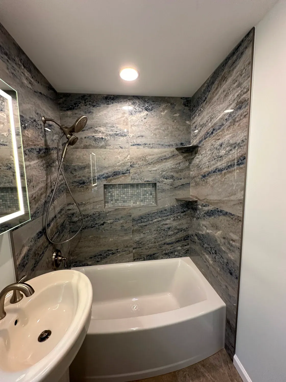 Bathroom with blue and tan marbled tile shower, white tub, and sink.
