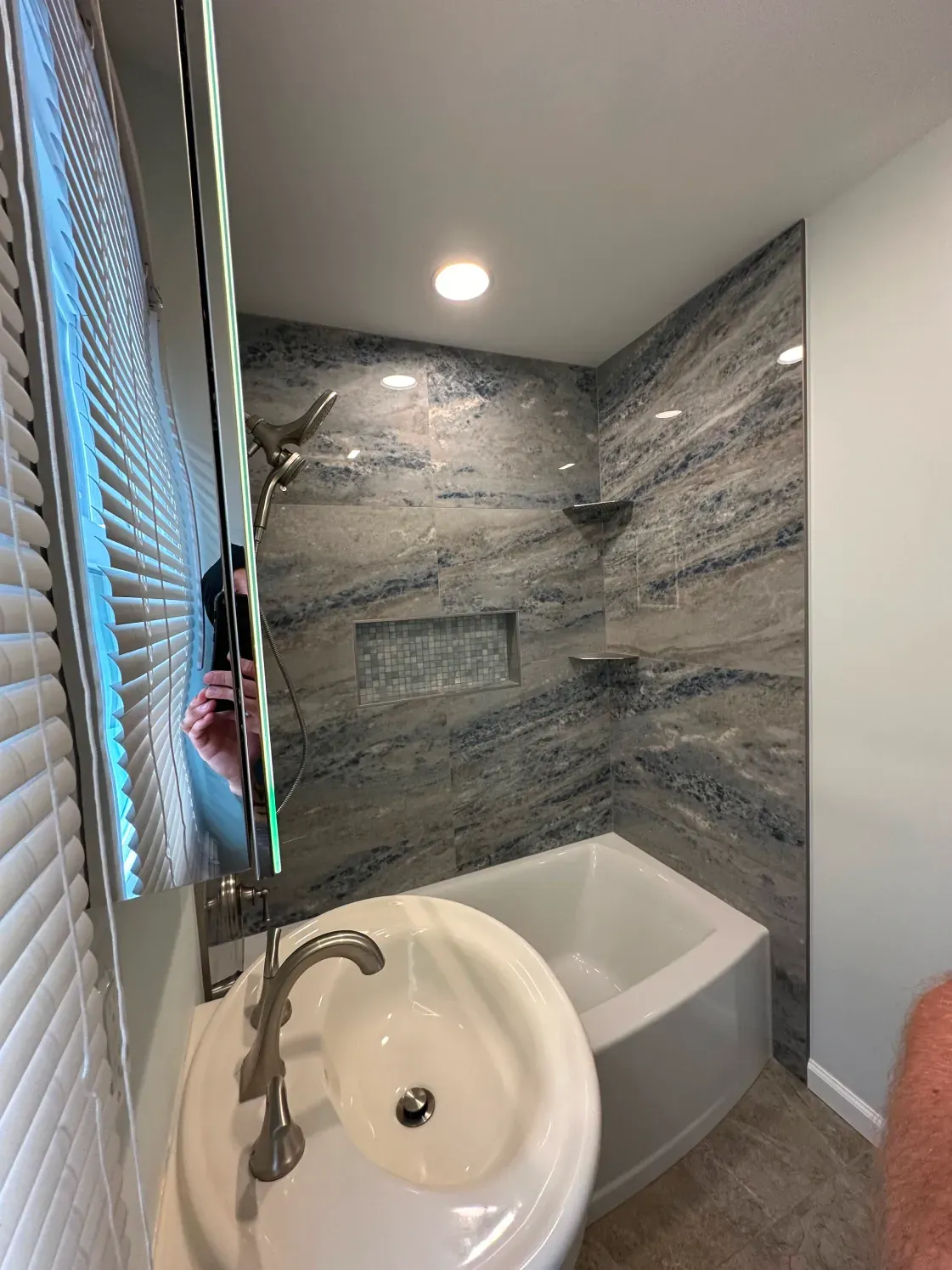 Bathroom with gray stone tile shower and tub. White sink. Large mirror.