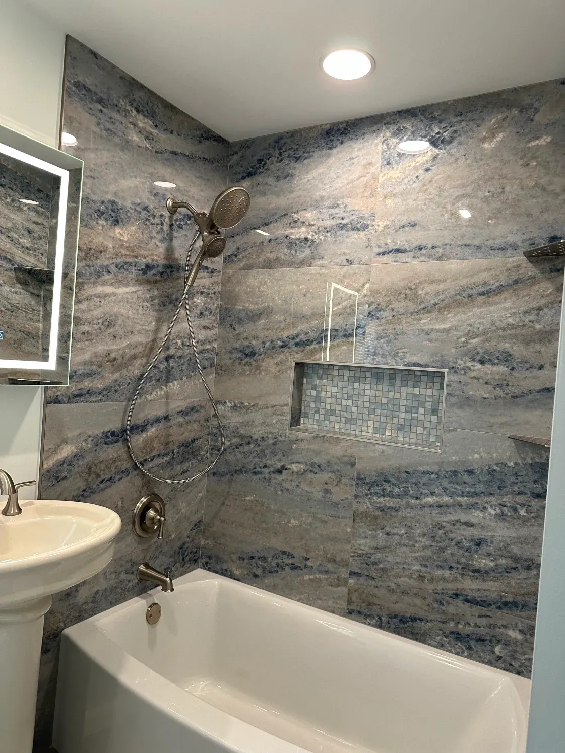 Bathroom with blue and grey tiled shower wall, white tub, and sink.