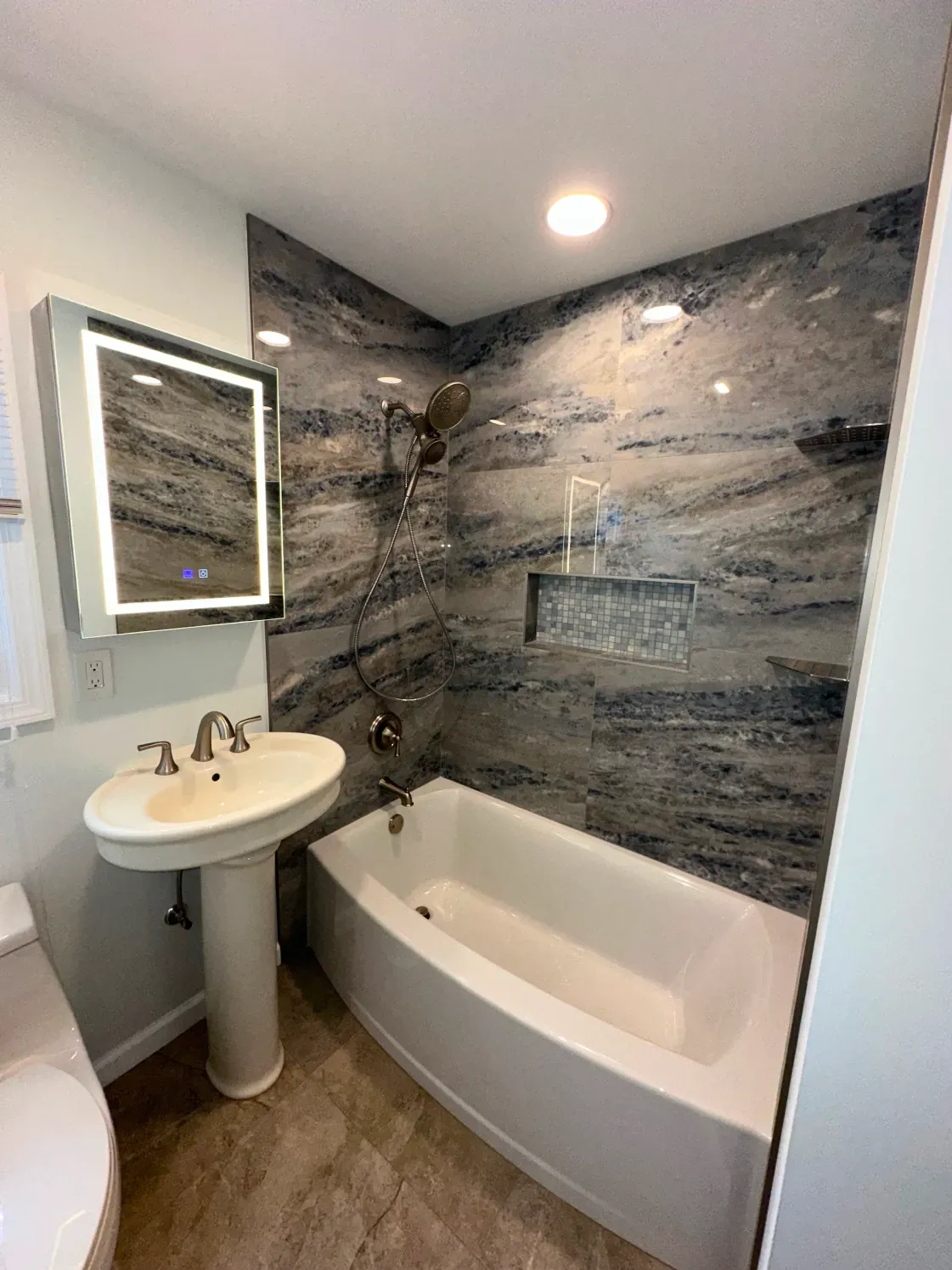 Bathroom with a white pedestal sink, bathtub, and gray marble shower wall.
