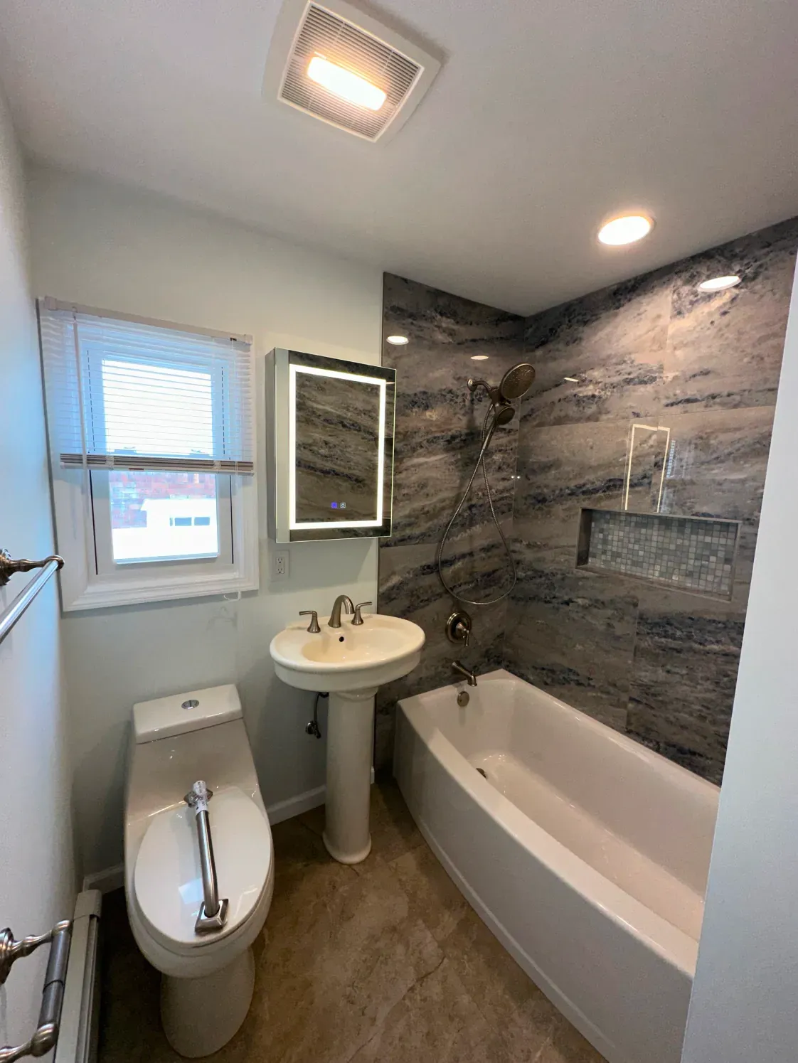 Small modern bathroom with white fixtures, gray accent wall, and a window.