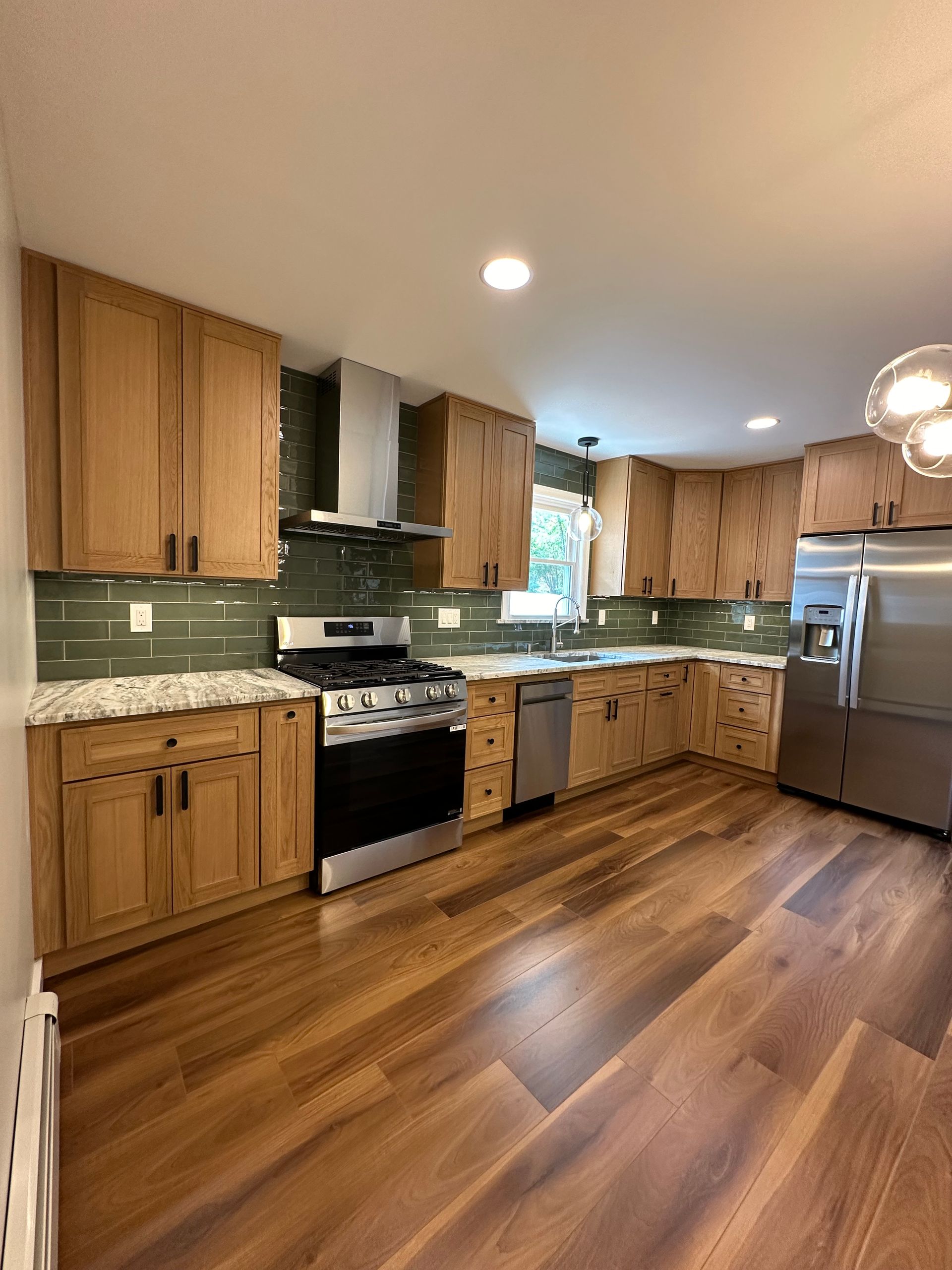 Kitchen with wood cabinets, stainless steel appliances, green backsplash, and hardwood floors.