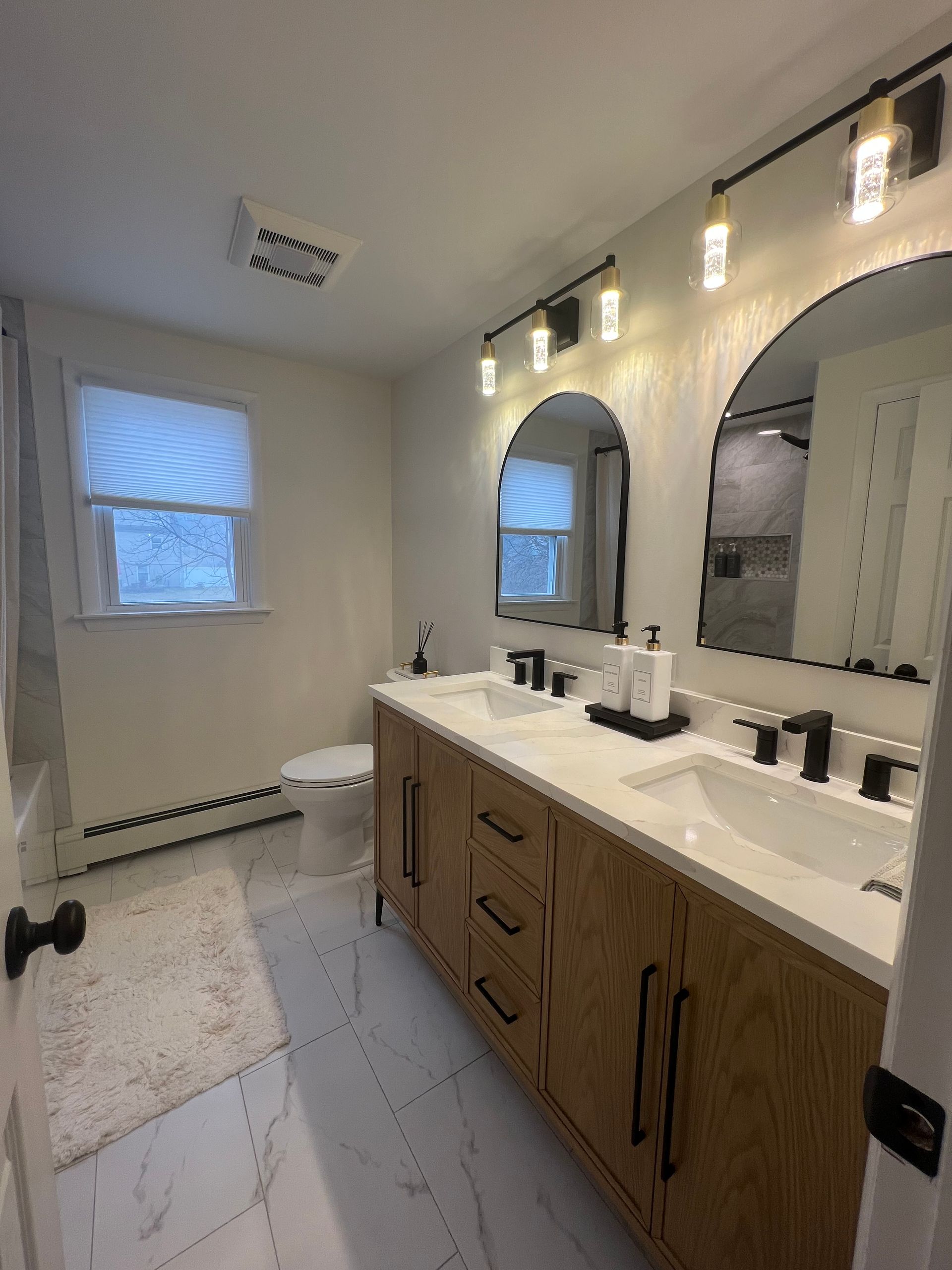 Bathroom with a wooden double vanity, arched mirrors, and marble flooring.