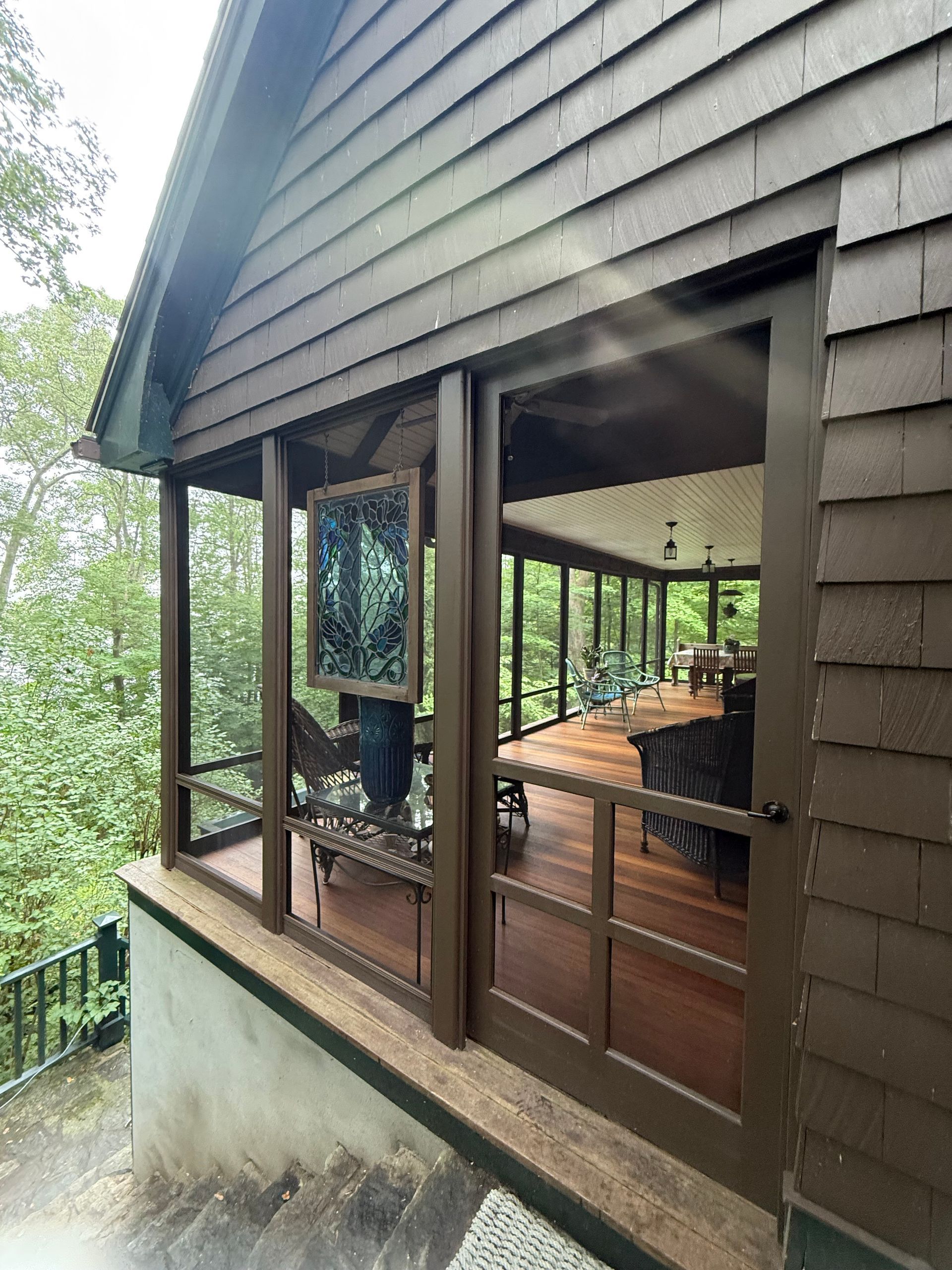 Brown cabin with screen windows overlooking a wooden deck and a lush green landscape.
