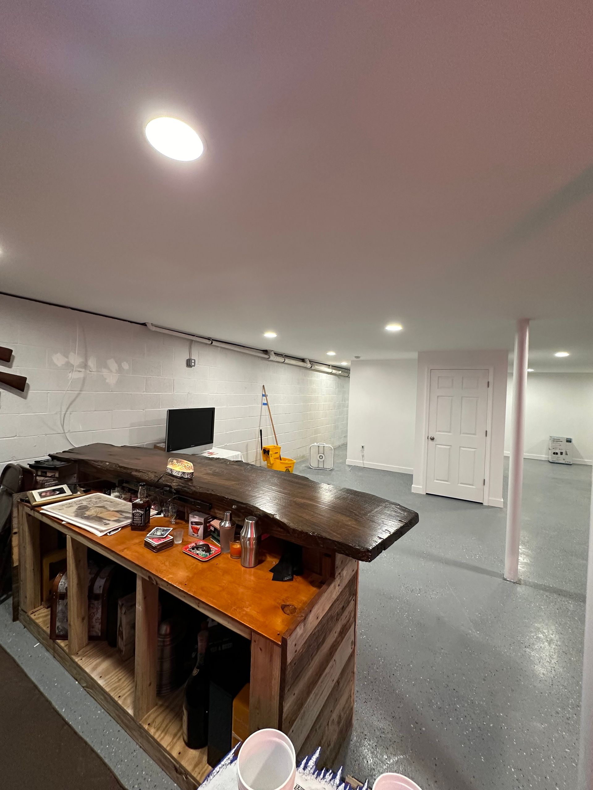 Basement bar with wooden countertop and shelving. Bottles, drinks, and a small TV are visible.