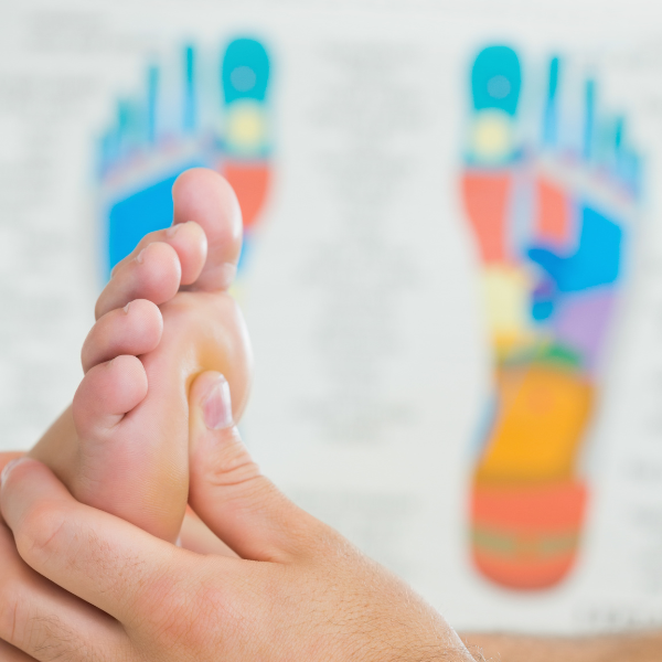 A person gets a reflexology massage with a reflexology map in the background.