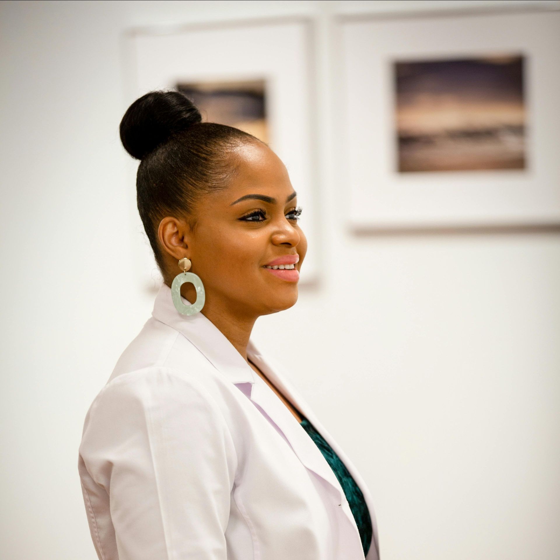 A woman wearing a white jacket and earrings is smiling