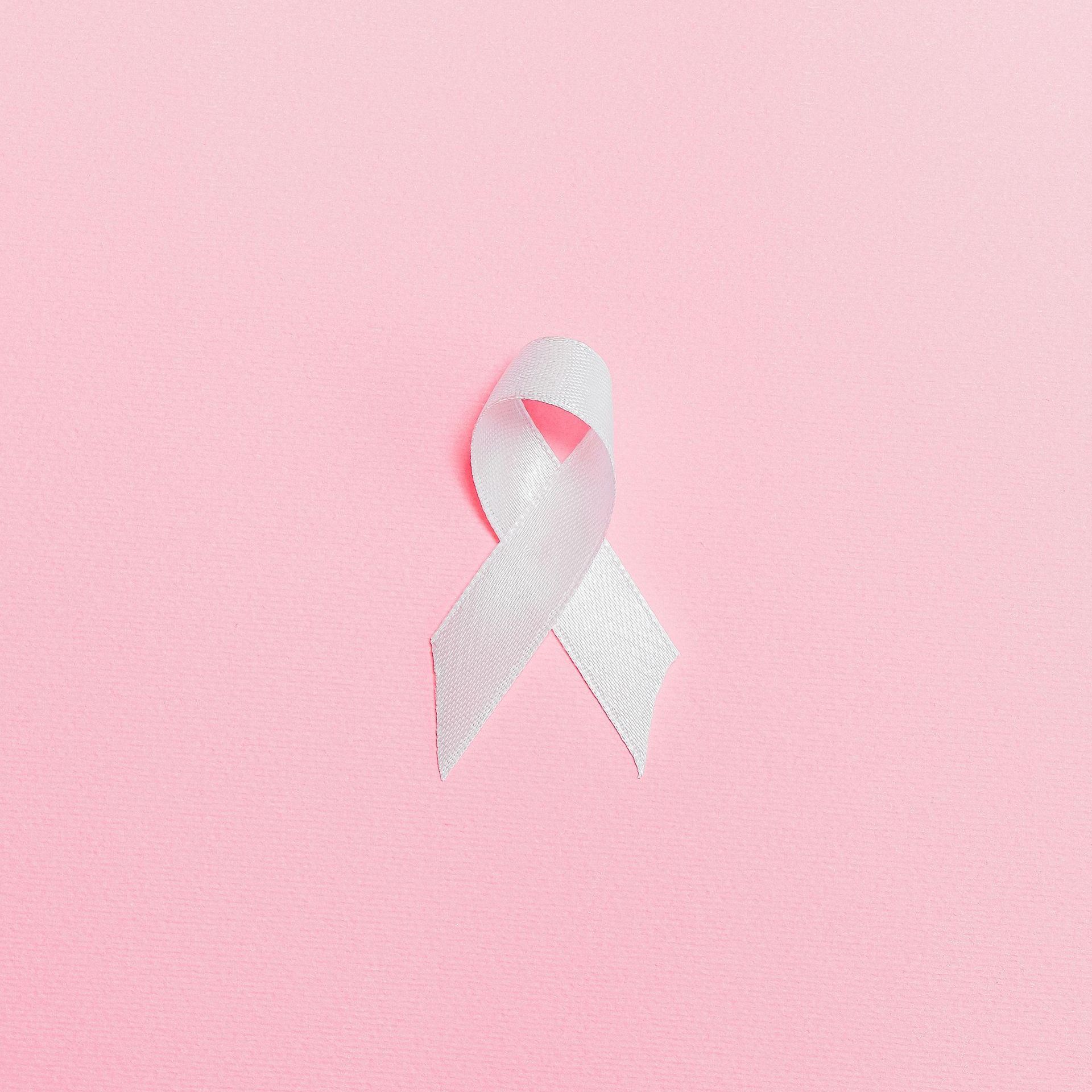 A white breast cancer awareness ribbon on a pink background.