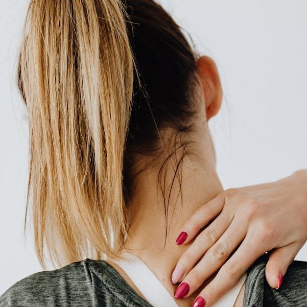 A young woman rubbing the back of her neck because it hurts/ Sandstone Therapeutic Massage