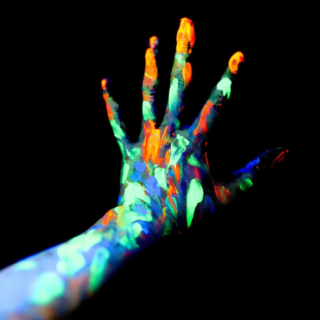 A person 's hand is painted with glow in the dark paint in UV light.