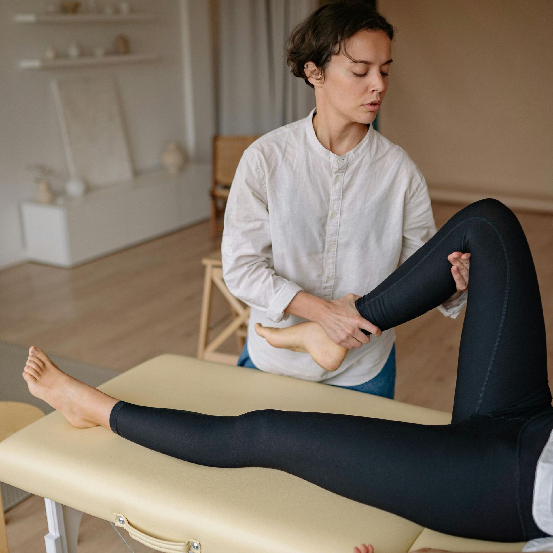 A massage therapist  is stretching a person's hips on a massage table. 