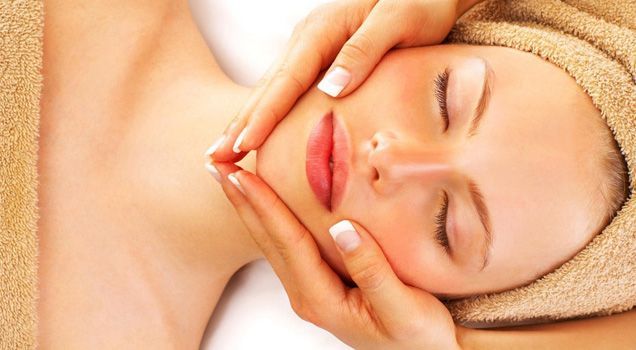 A woman with a towel wrapped around her head is getting a facial massage.