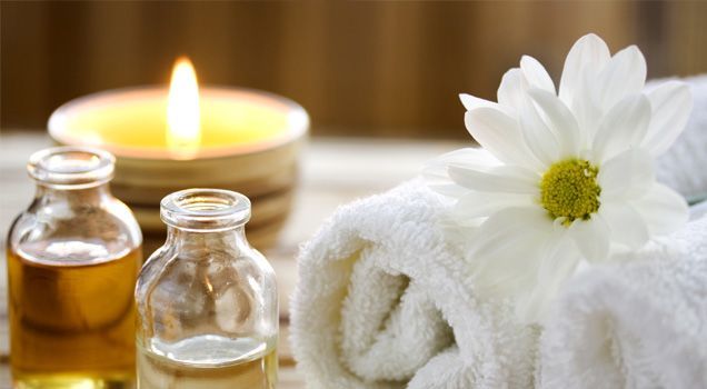 A candle , towels , bottles of oil and a flower on a table.