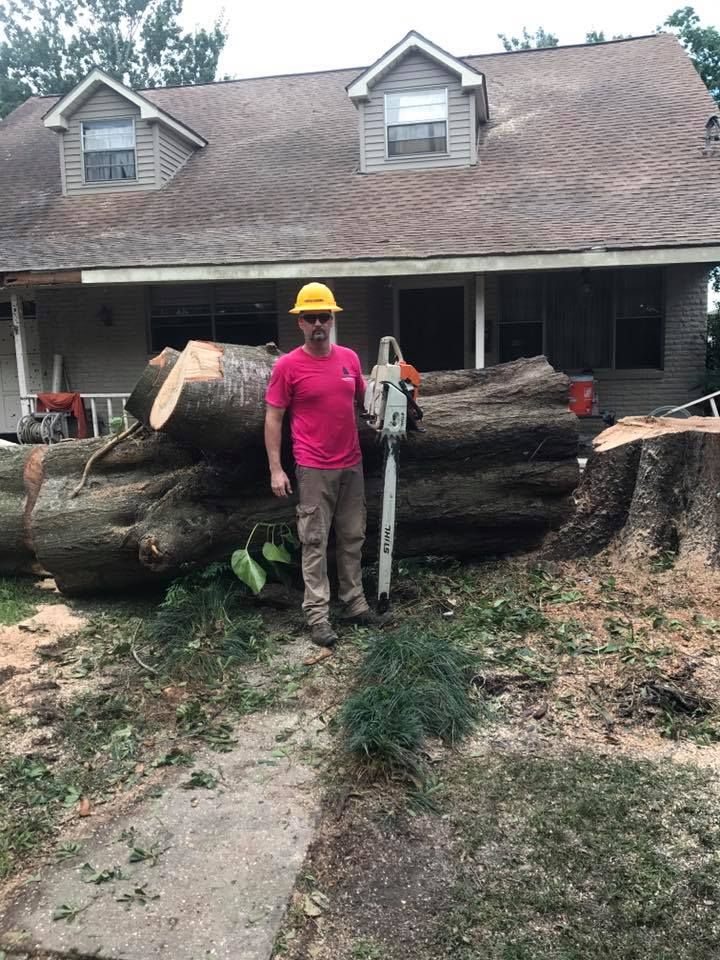 A man is standing in front of a house holding a chainsaw.