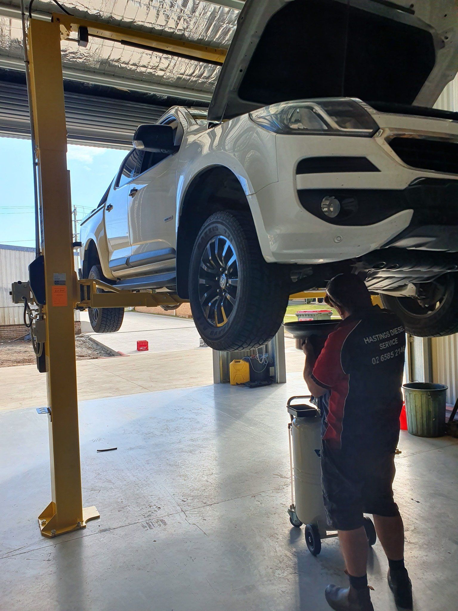 A Man Is Working Under A Car In A Garage — Hastings Diesel Service In Wauchope, NSW