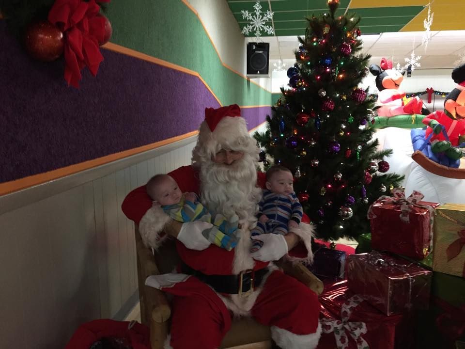 Two babies are sitting on santa 's lap in front of a christmas tree