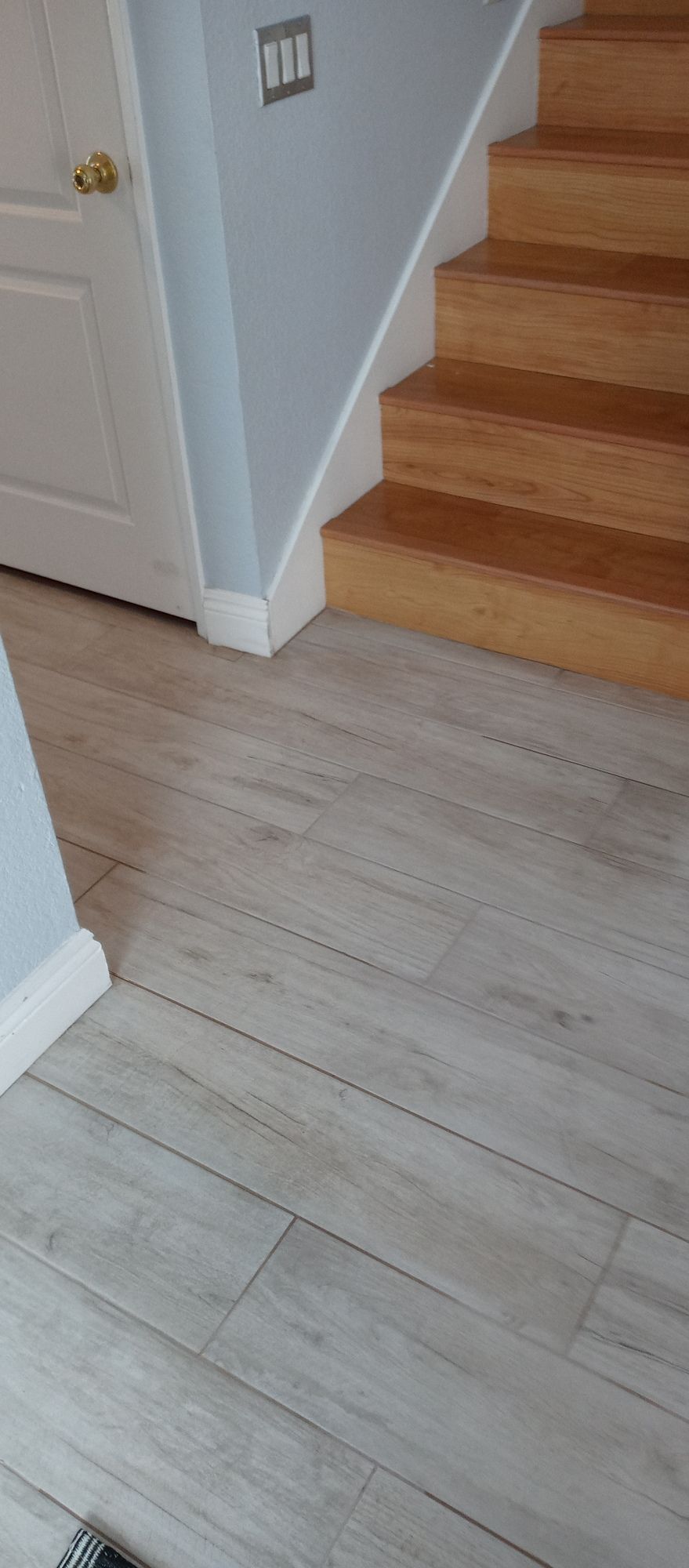 A close up of a wooden staircase with a white tile floor.