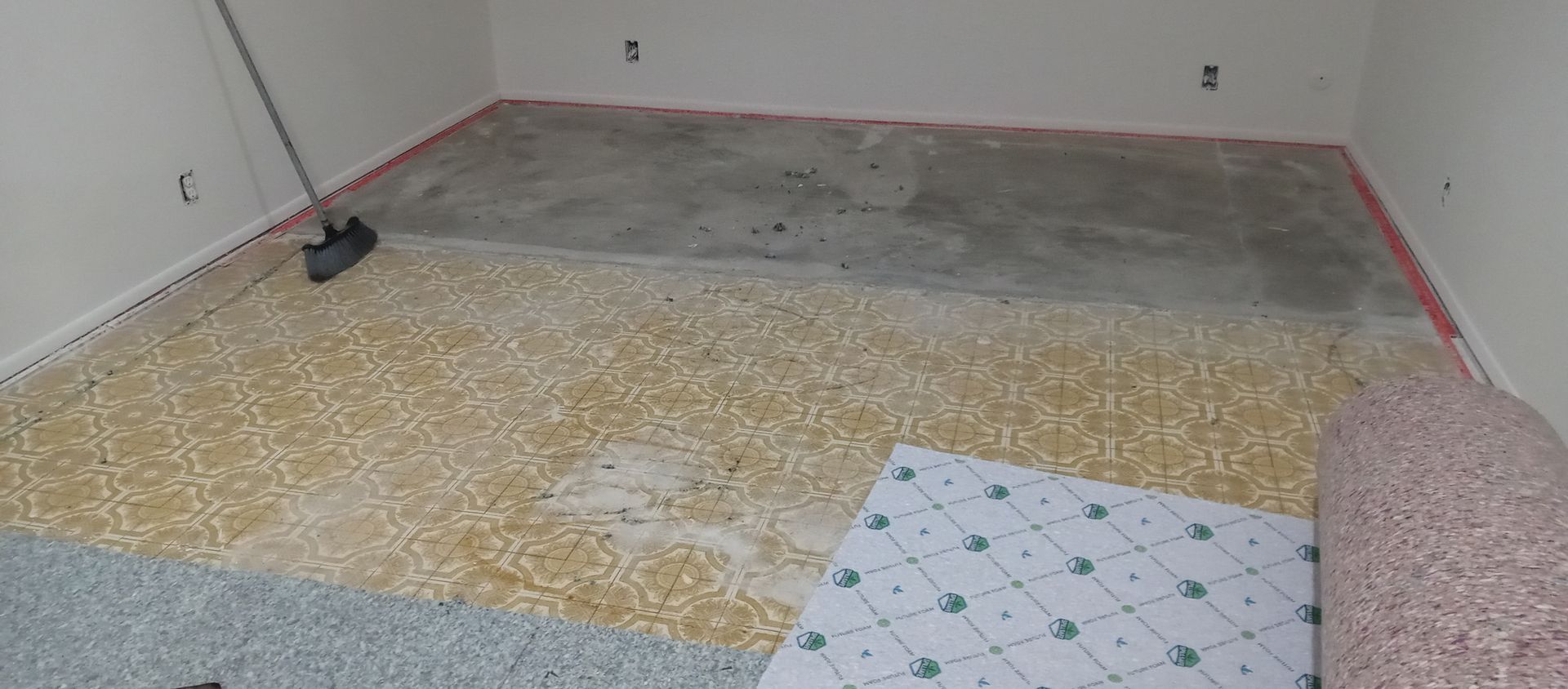 A room with a broom and a piece of carpet on the floor.