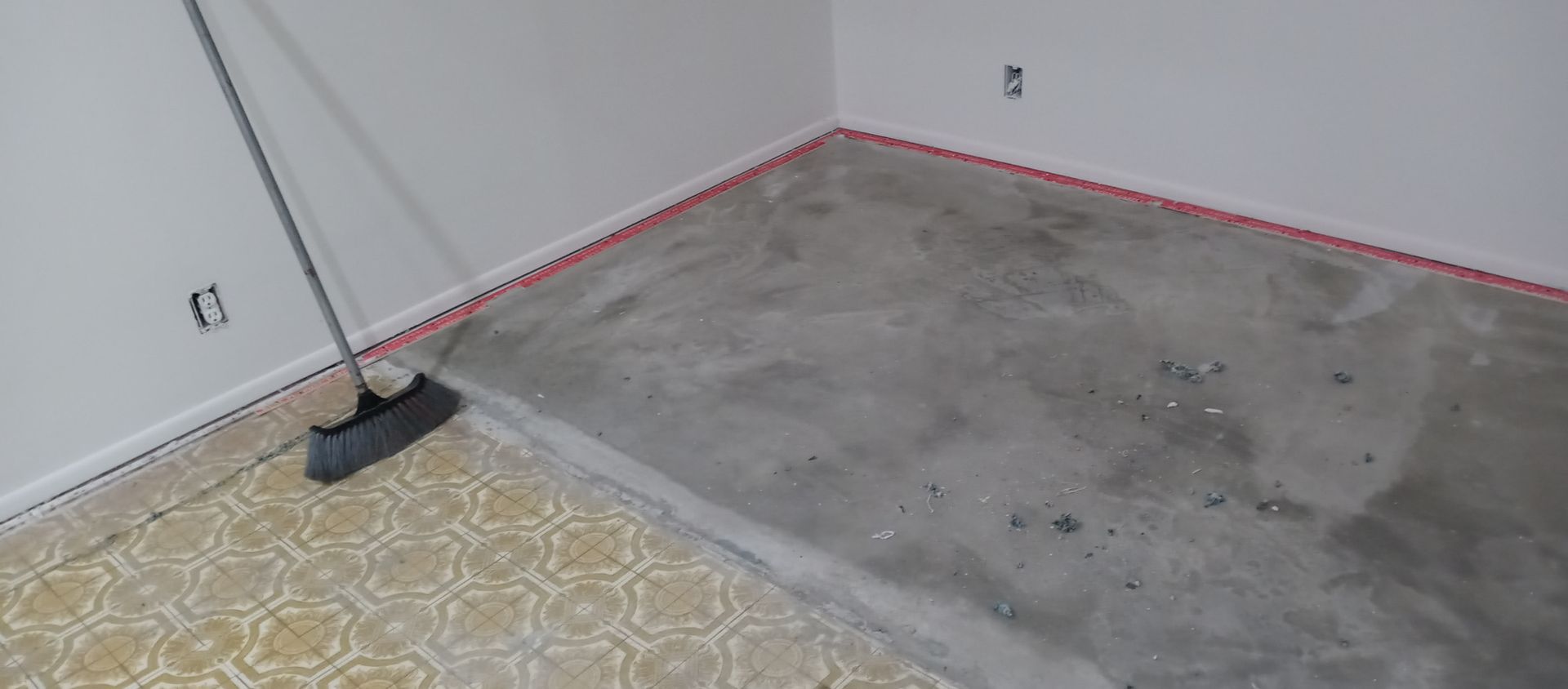 A broom is sitting on a concrete floor in a room.
