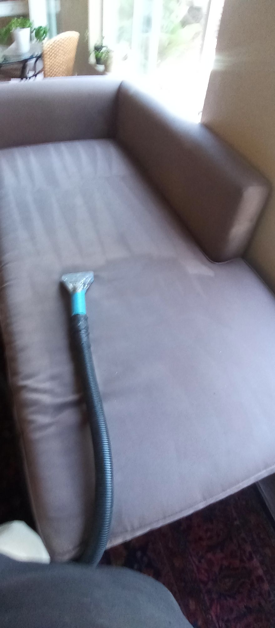 A vacuum cleaner is being used to clean a couch in a living room.