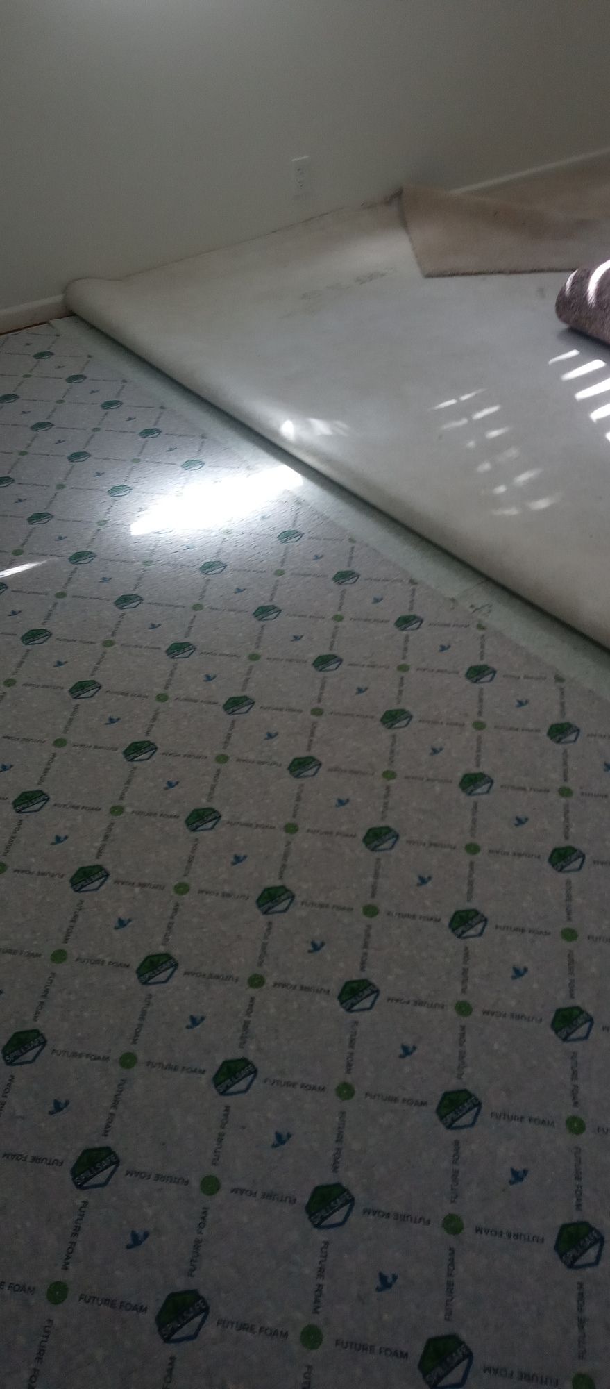 A person is laying a carpet on the floor in a room.