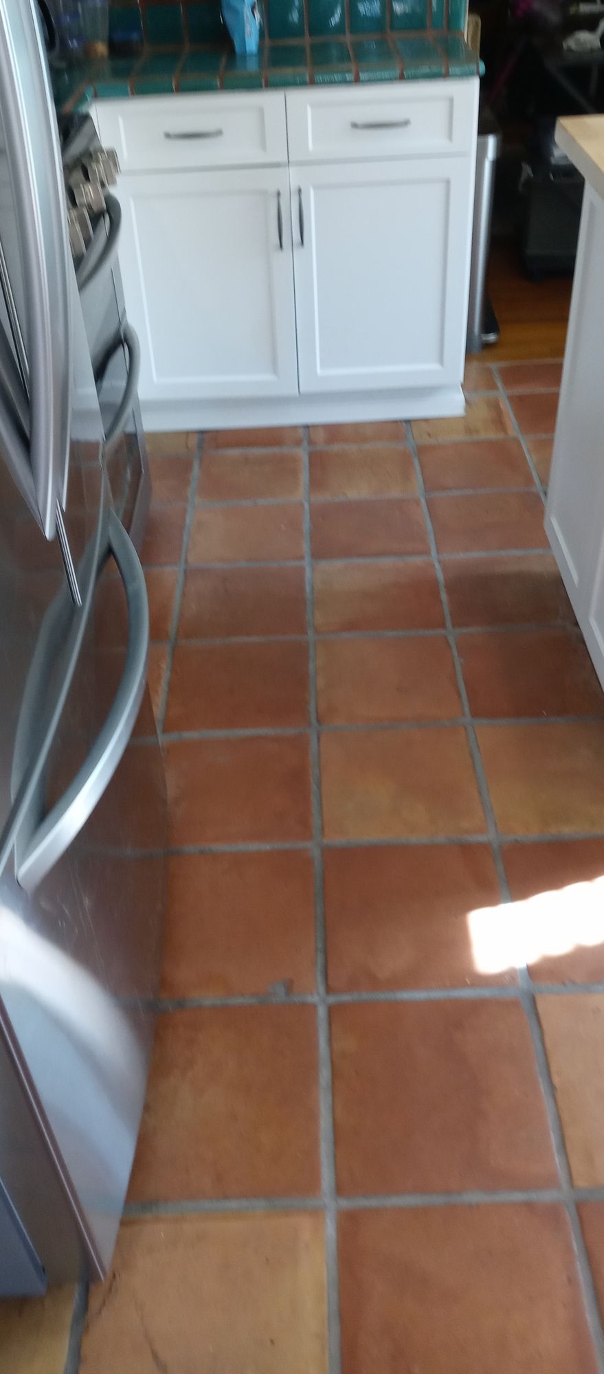 A kitchen with red tile floors and white cabinets.