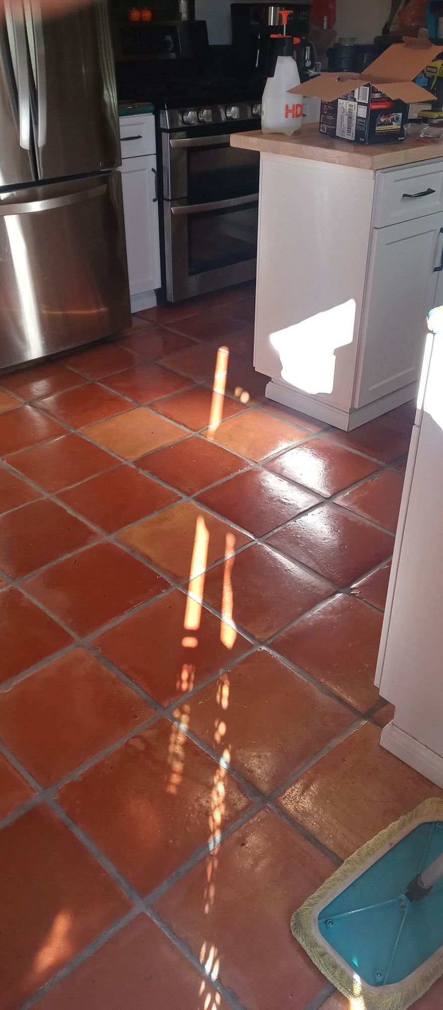 A kitchen with red tile floors and a stainless steel refrigerator.
