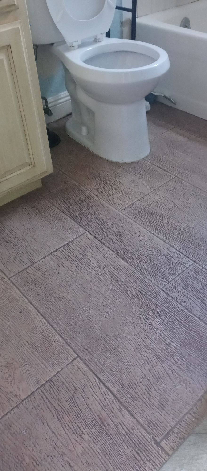 A toilet is sitting on a tiled floor in a bathroom next to a bathtub.