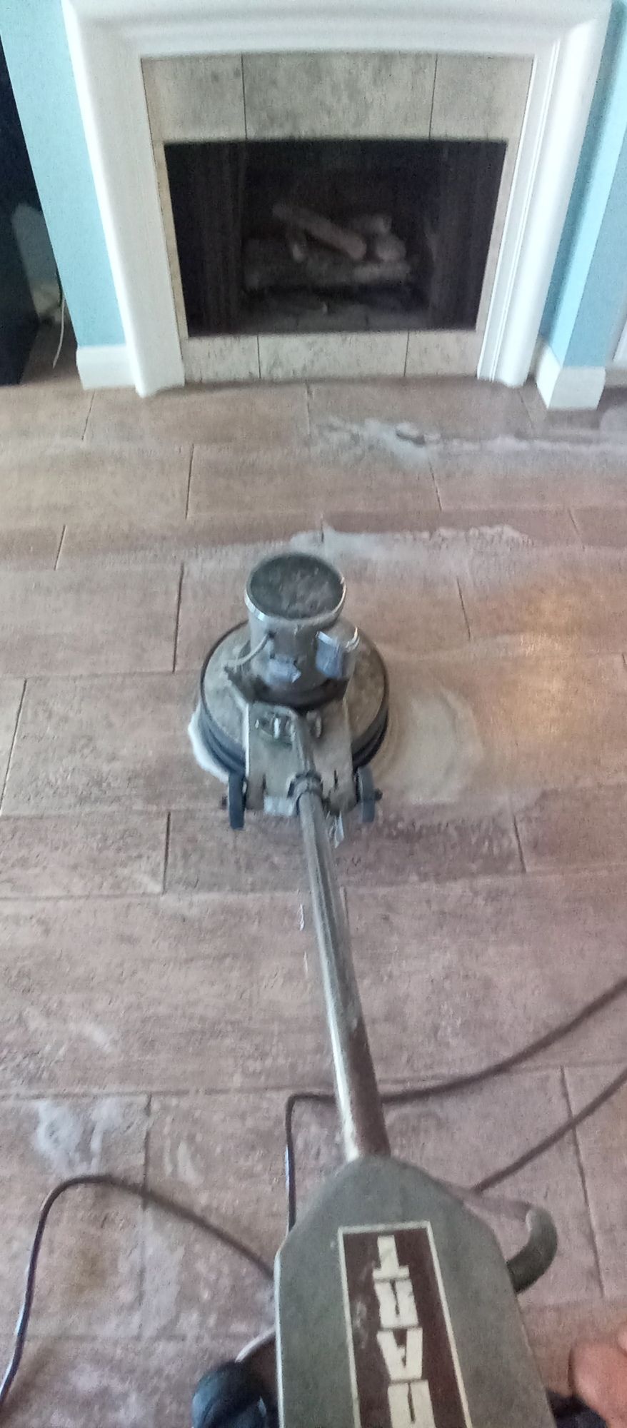 A person is using a machine to polish a wooden floor in a living room.