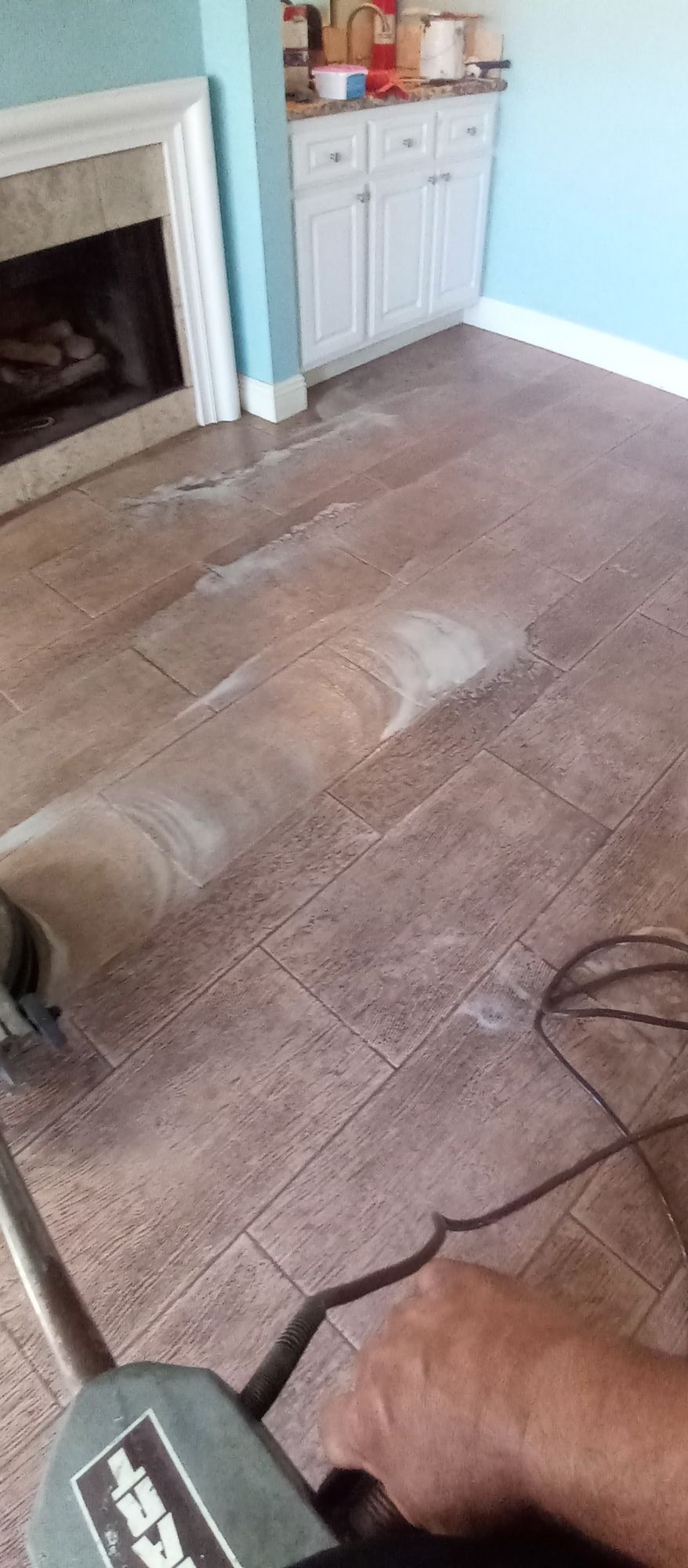 A person is using a machine to sand a tile floor in a living room.