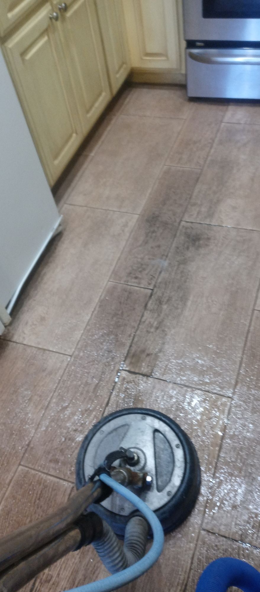 A person is cleaning a tile floor in a kitchen with a machine.