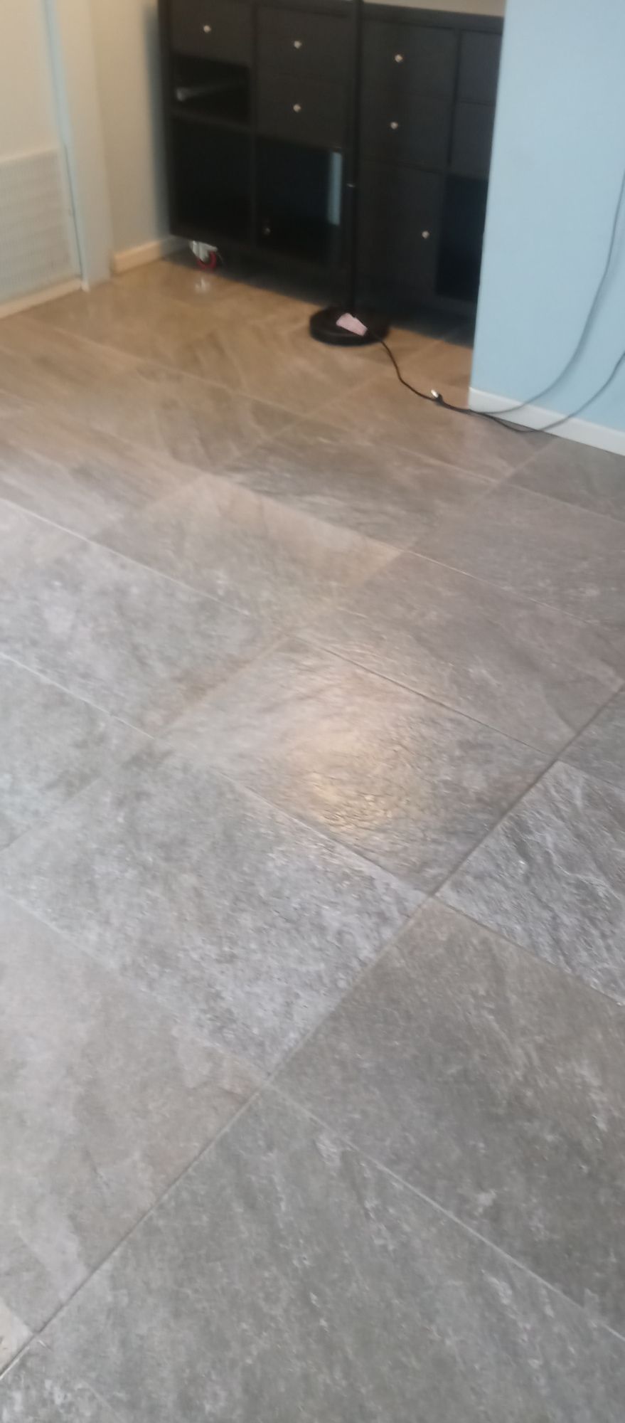 A gray tile floor in a living room with a tv stand in the background.
