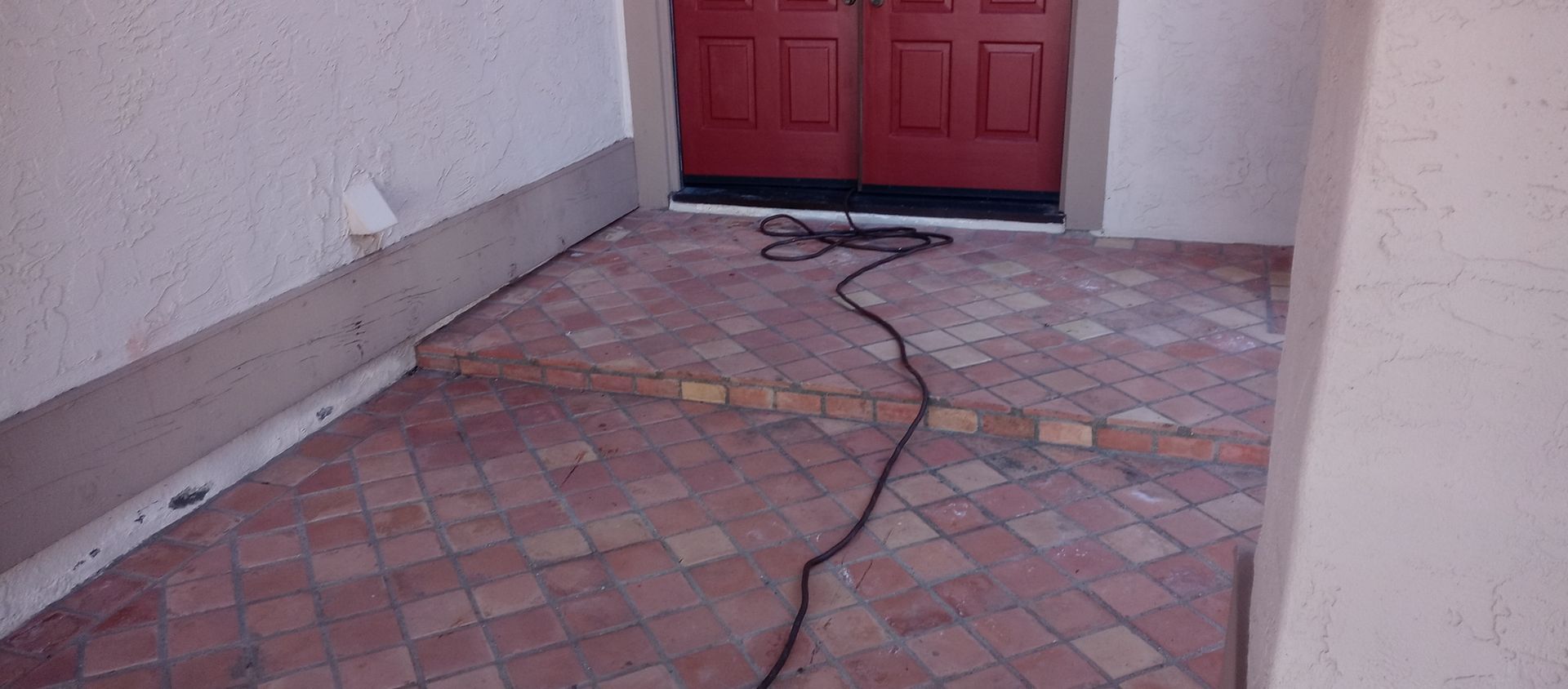A brick walkway with a red door and a power cord.