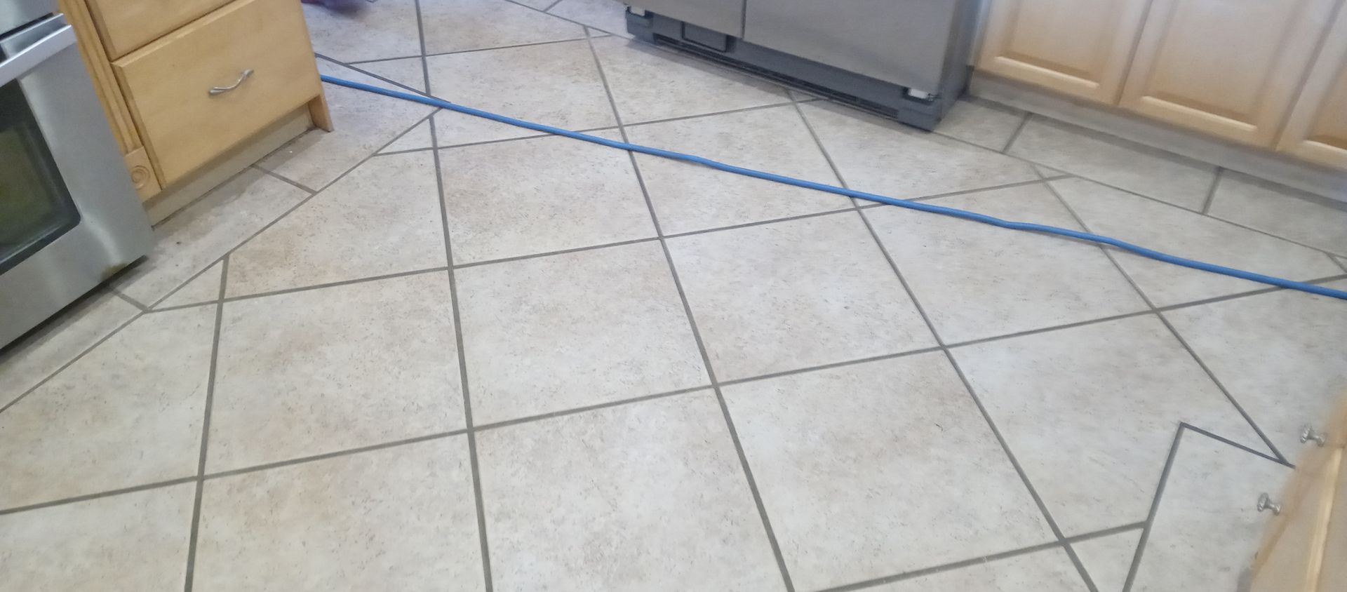 A tiled floor in a kitchen with a blue line going through it.