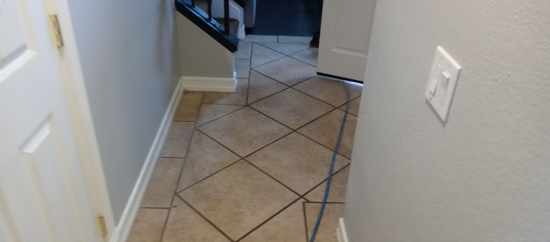 A hallway with a tiled floor and stairs in the background.