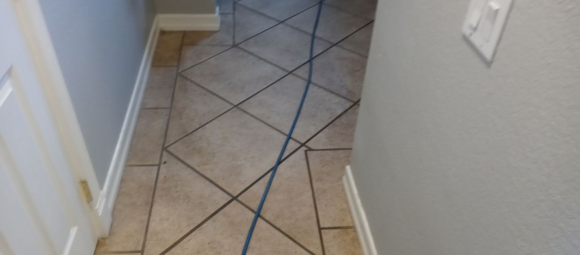 A tiled floor in a hallway with a vacuum cleaner attached to it.