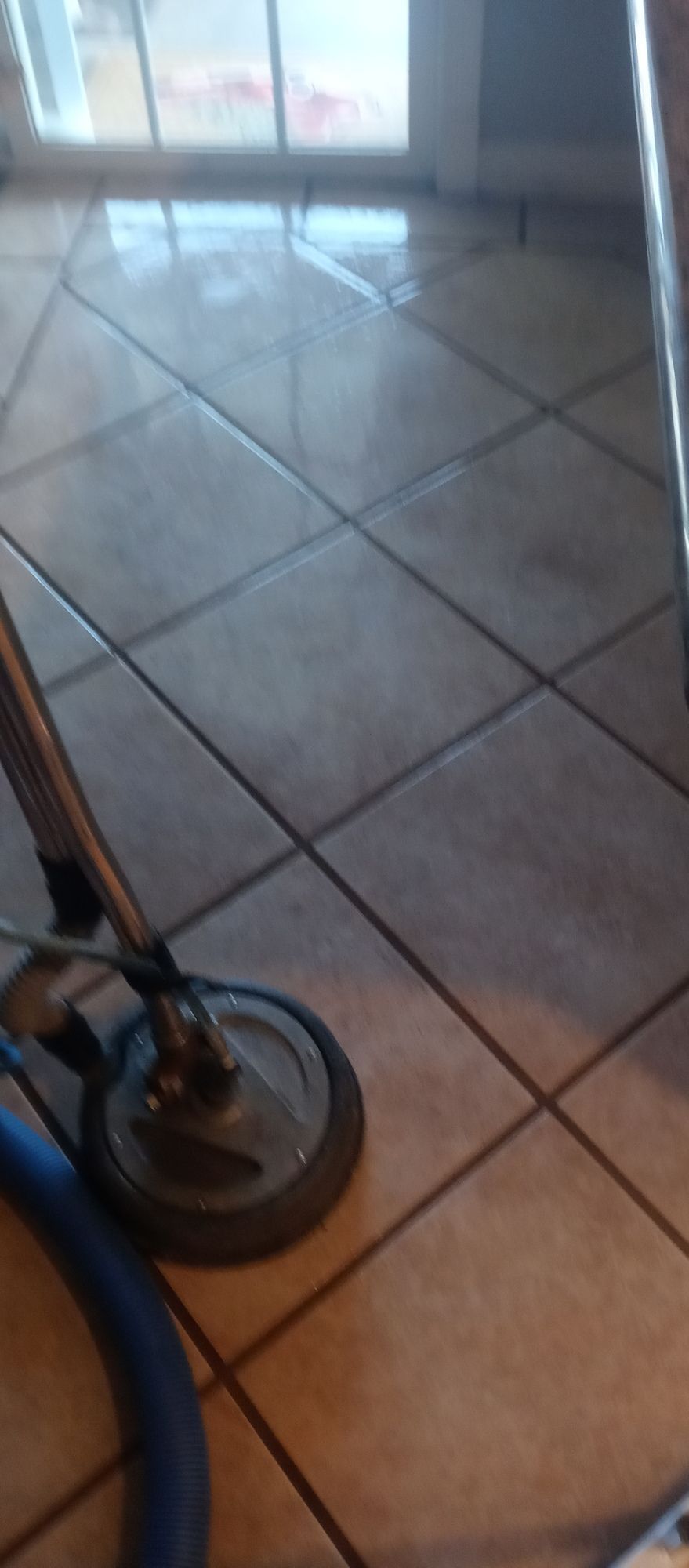 A vacuum cleaner is cleaning a tile floor in a kitchen.