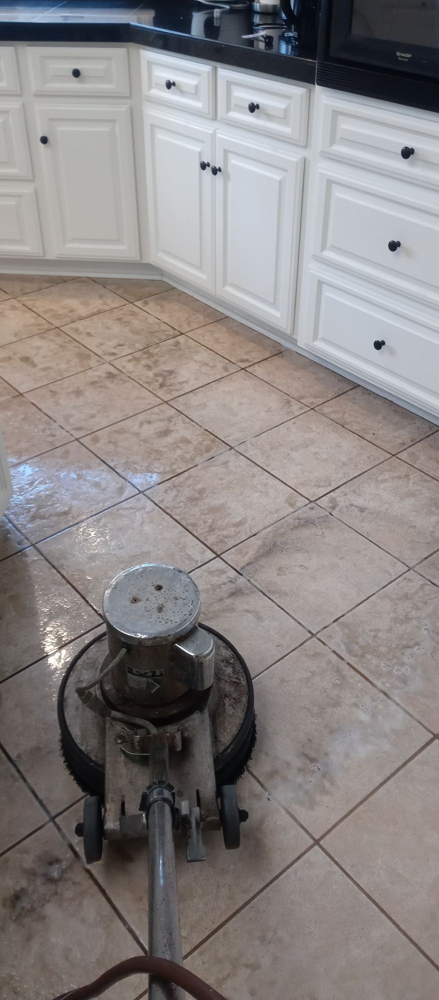 A tile floor is being cleaned in a kitchen with a machine.