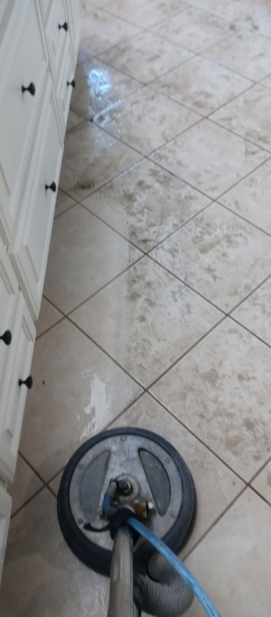 A tile floor is being cleaned with a machine in a kitchen.