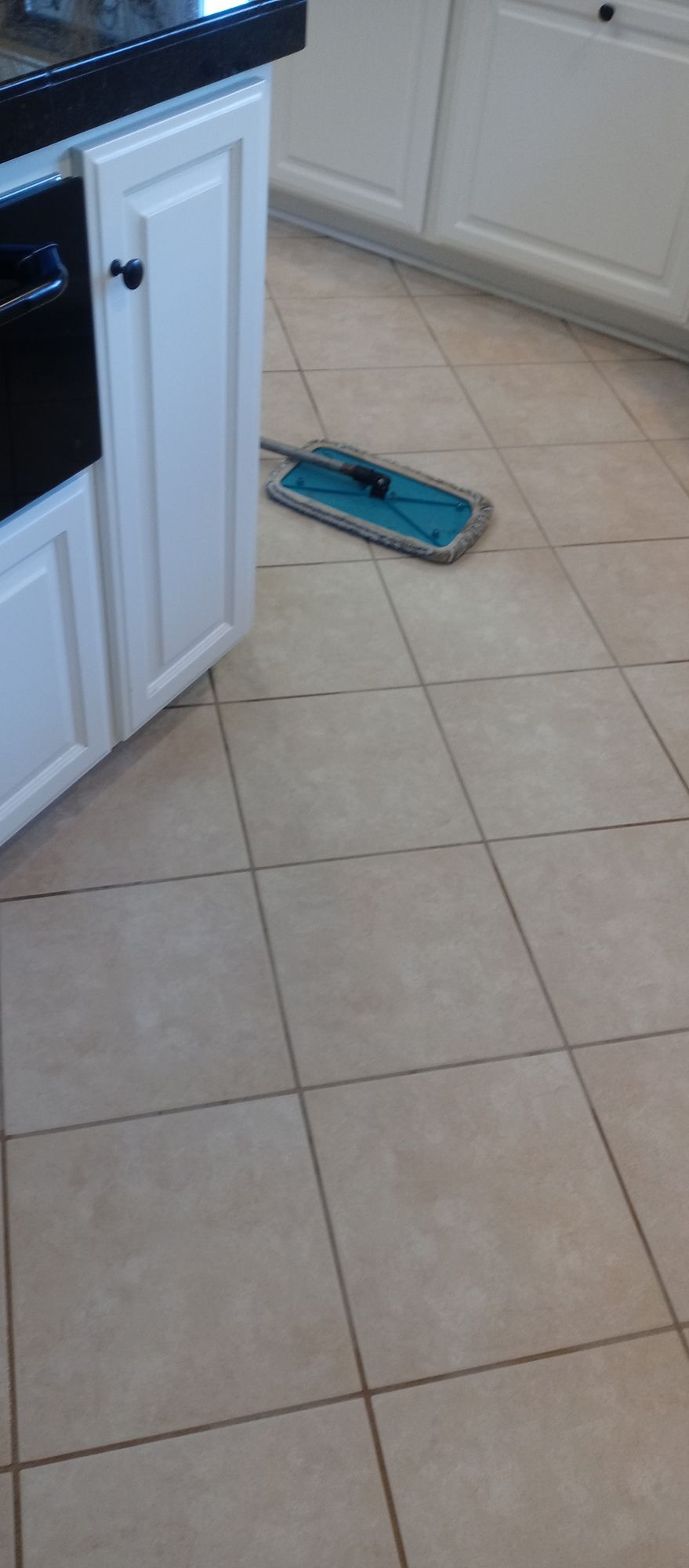 A mop is sitting on the floor of a kitchen next to a cabinet.
