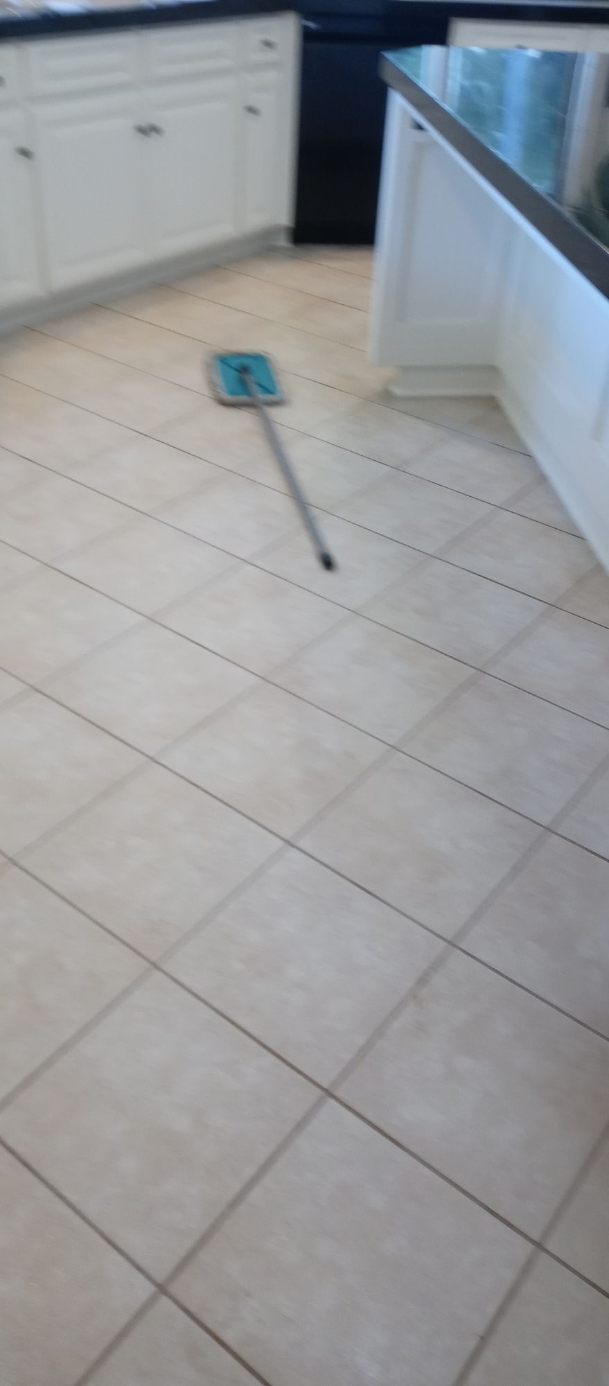 A mop is sitting on a tiled floor in a kitchen.
