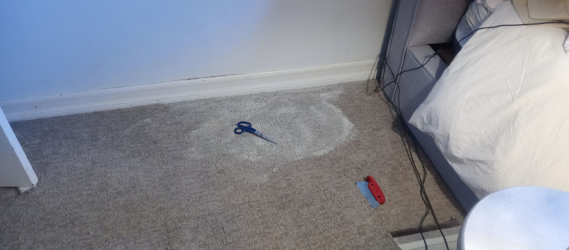 A key is laying on the floor next to a bed.