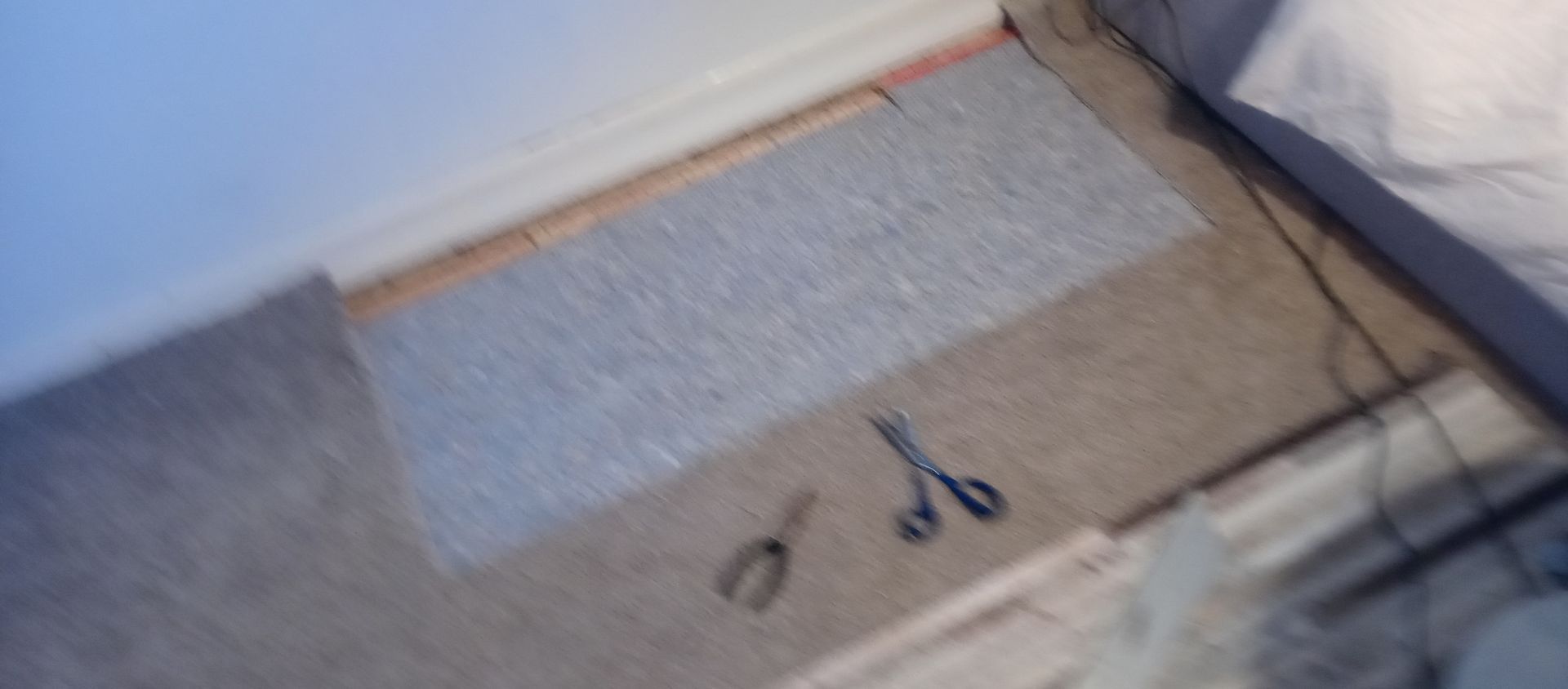 A pair of scissors are laying on the floor next to a bed.