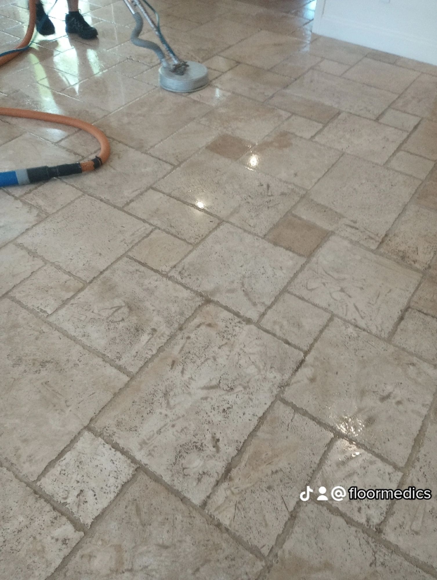 A person is cleaning a tile floor with a vacuum cleaner.